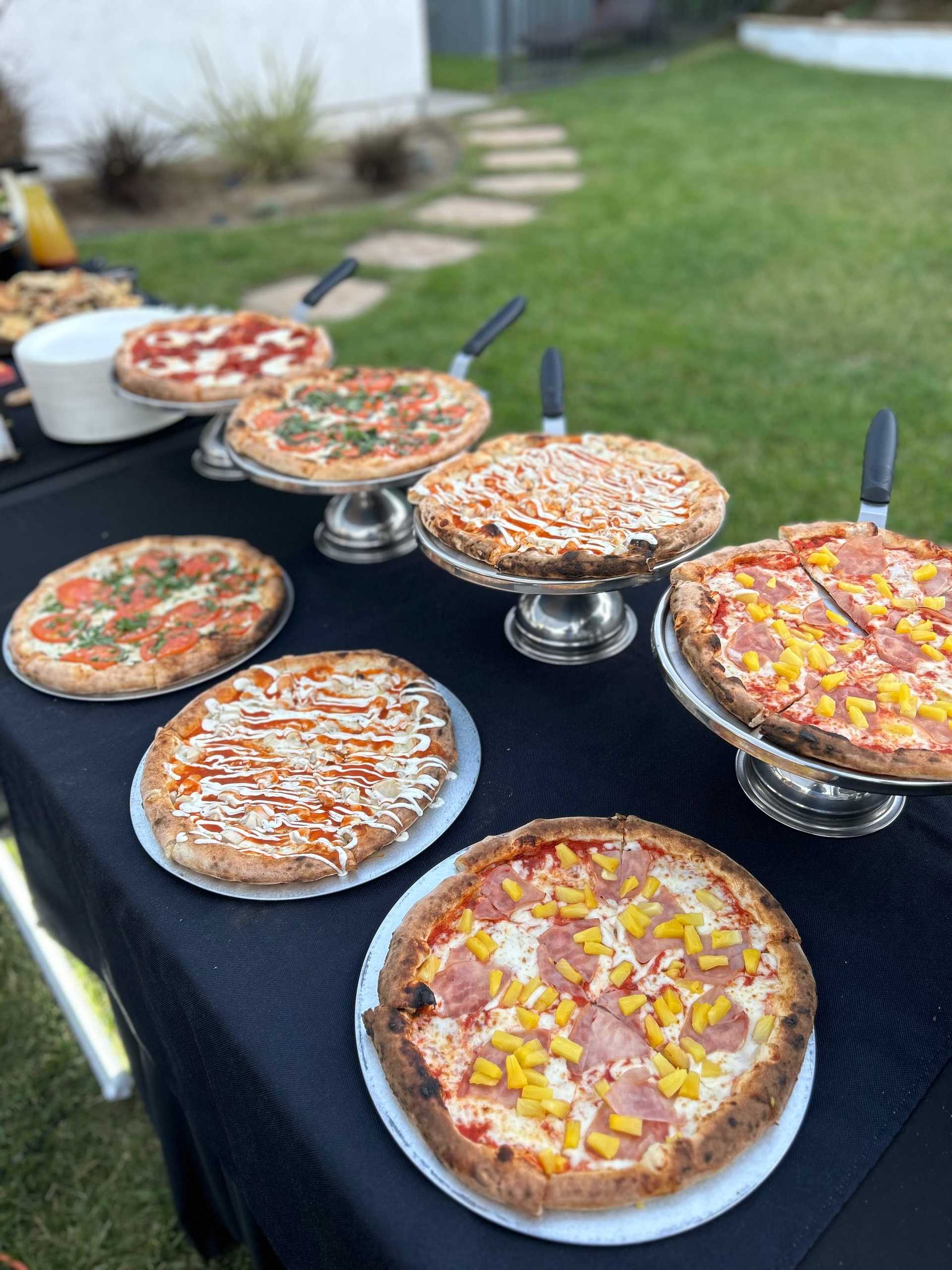 An assortment of pizzas with different toppings on a table set outdoors.